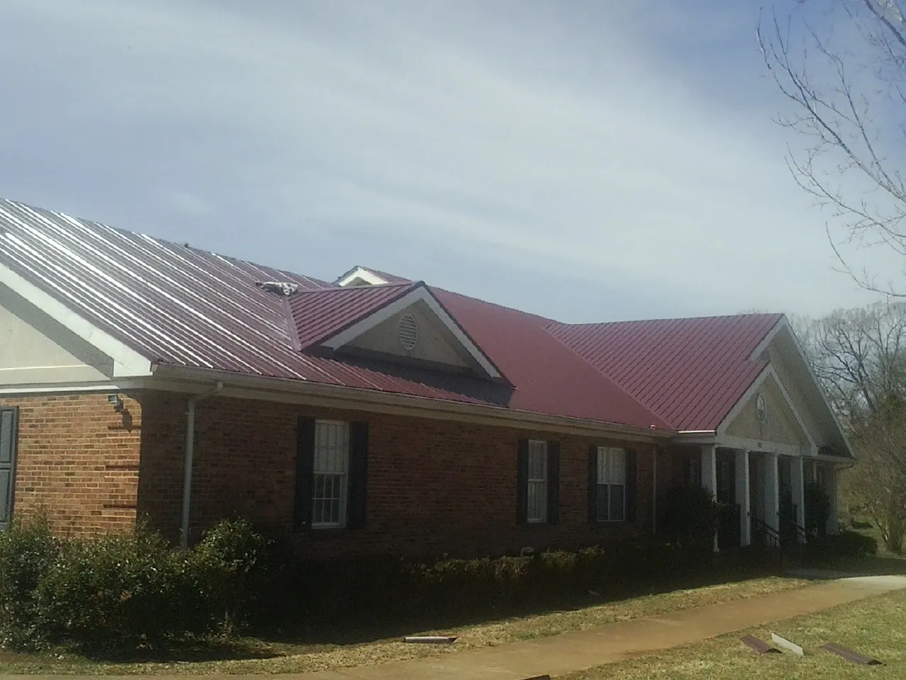 Red metal roof with gabled entries on a long brick building, from a Hail Damage Roof Repair job in Derby