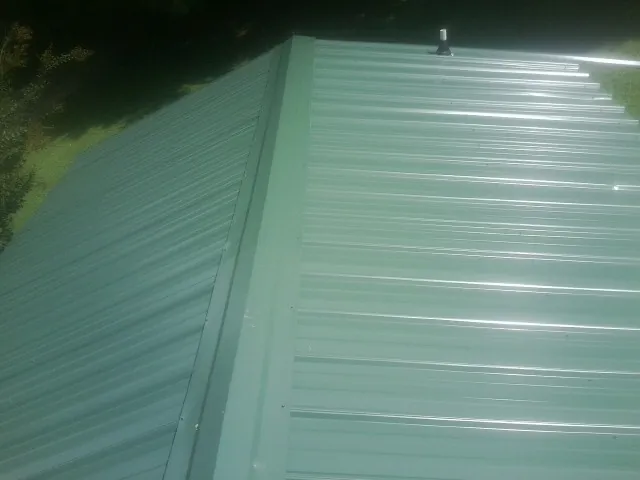 New green metal panels meeting at the ridge of a roof — Flat Roof Repair work by our crew in Derby